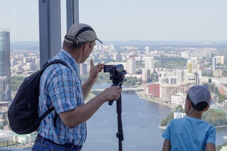 A boy and his grandfather are standing at the panoramic window of a high-rise building looking at the city of Yekaterinburg, Russiaの写真素材