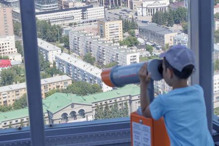 Focus on the city of Yekaterinburg. The boy looks into a telescope from a panoramic window of a high-rise building. The image of the boy is blurred. Inscription Ural State Universityの写真素材