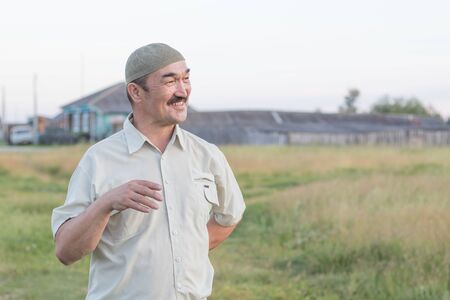 A Muslim senior man is standing and talking about something fun. Siberian village.の写真素材
