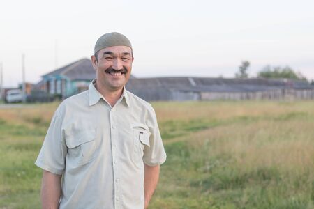 Muslim senior man stands and laugh good-naturedly against the background of the Siberian villageの写真素材