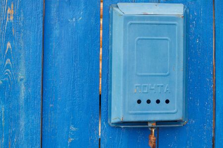 An old blue Soviet mailbox with the inscription Mail and a rusty lock hanging on a rural wooden blue fence. Close-up.の写真素材