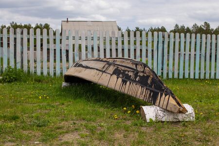 New wooden tarred boat of pine lies upside down in a clearing near the fence.の写真素材