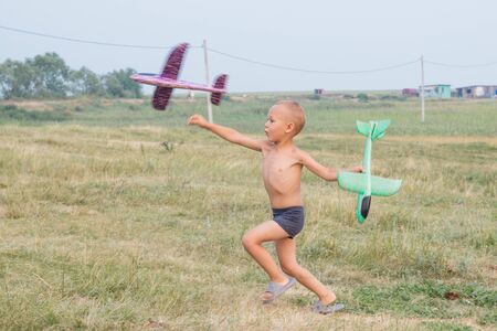 Cute little boy in shorts runs across the field and launches a toy airplane.の写真素材