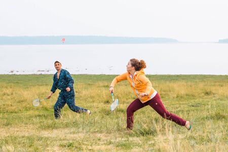 Young couple play badminton on the lake. The girl runs and prepares to beat off a shuttlecock with a racket.の写真素材