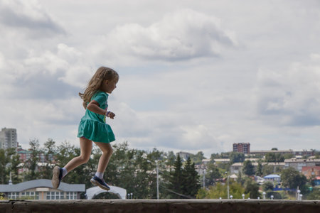 A little girl runs through the air against the background of the city and clouds.のeditorial素材