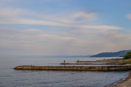 Lake Baikal. On breakwaters, fishermen catch fish with fishing rods. Evening landscape.