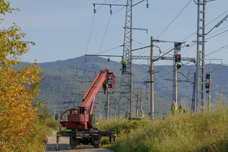 Workers repair the support of the high-voltage line of the railway using a special machine with a...