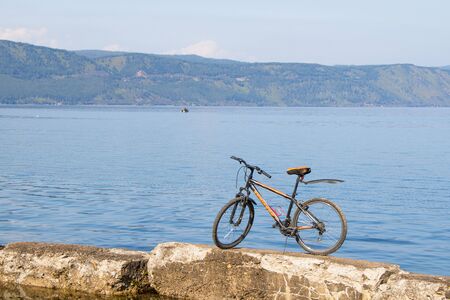 Bicycle standing on stones against backdrop of Lake Baikal. Copy spaceの写真素材
