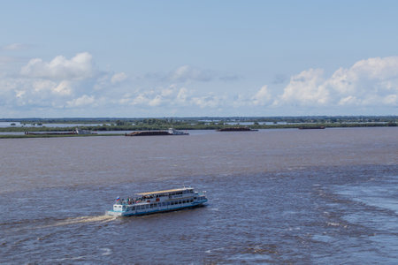 Walking excursion river ship with tourists moves along Amur River. Water level in river is higher than normal. Flooded shores are visible on opposite side.のeditorial素材