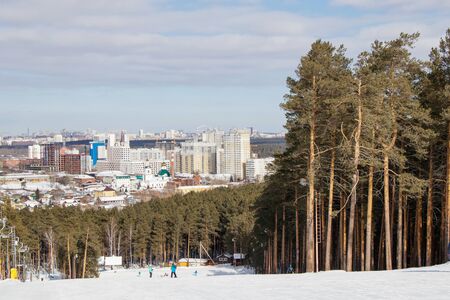 The training slope of the sports complex on Uktus Mountain framed by a pine forest. In the background a panorama of the city of Yekaterinburg, Russiaの写真素材