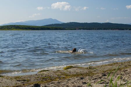 The picturesque lake Tunaicha. The girl swims in the water near the shore, creating a spray. Motion blur. Near Sunny Beach, Sakhalin Island, Russiaの写真素材