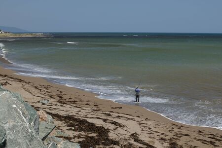A fisherman fishing with a fishing rod on the coast of the Sea of Okhotsk near the village of Okhotsk.の写真素材
