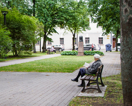 Daugavpils, Latvia - July 4, 2018: Senior woman is sitting on a bench in a city park and reading a book.のeditorial素材