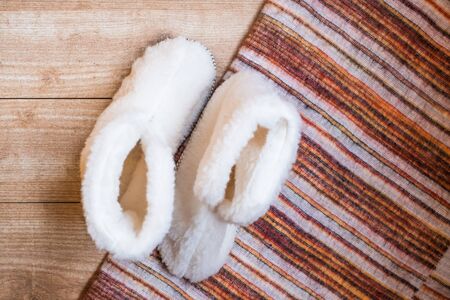 Cozy homemade white faux fur boots and striped woolen plaid on a wooden background. Hygge concept....