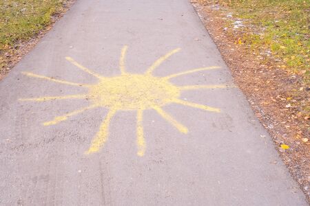 Sun with rays drawn in yellow chalk on the sidewalk in a city autumn park.の写真素材