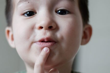 Adorable little asian boy put his finger to his lips and looks down at camera. Close up.の写真素材