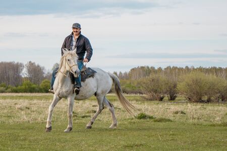 Rider on a white horse rides through the pasture.の写真素材