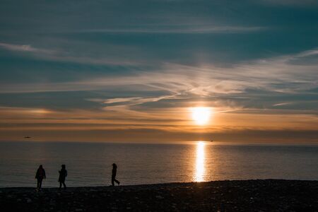 Impressive beautiful winter sunset on the Black Sea, Russia. Silhouettes of 3 persons walking along the shore.の写真素材