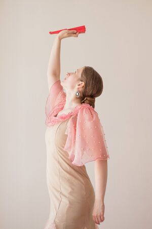 Portrait of a beautiful young woman in a beige and pink dress on a beige background. She is dancing flamenco. A hand with a red fan is raised up.の写真素材