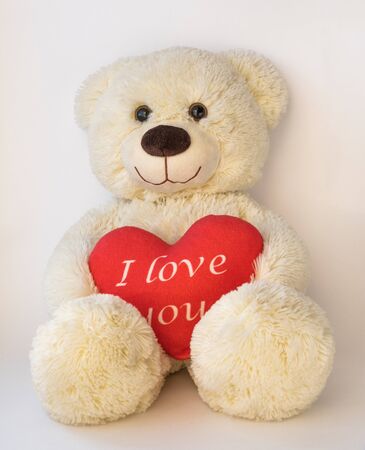 Cute teddy beige bear sitting on a white background. He holds a big red heart with the text. I love youの写真素材