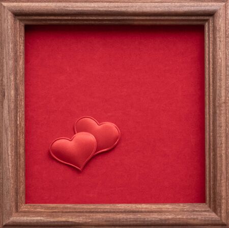 Valentines day card flat lay top view. 2 small textile red hearts are nearby on a background of red velvet paper in wood square brown frame. love wedding concept. Copy space place for textの写真素材