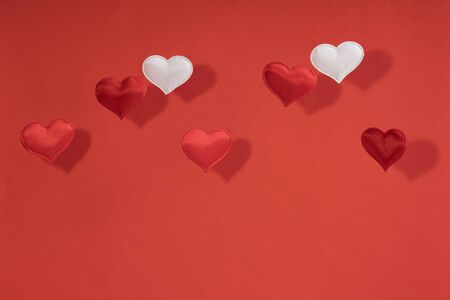 Valentines day card. 2 white and 5 red flying small textile hearts and their shadows are on a...