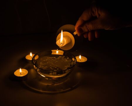 Ancient fortune telling on wax and water. On a black background, the hand holds a candlestick with a burning candle over a cup of water. A drop of hot wax on the edge of the candle. Divination conceptの写真素材