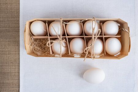 9 natural fresh white eggs in eco-friendly wooden packaging and one egg separately on a white napkin.の写真素材