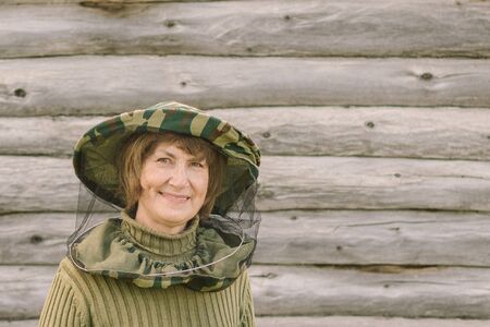 Close up portrait of a pretty woman beekeeper in protective green mask on a background of a log wall. She is looking at the camera and smiling. Siberian village, Russiaの写真素材