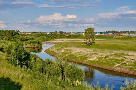 Summer landscape on a sunny day. Neighborhood of the Siberian village Begitino, Tyumen region, Russia. Vagai river, lonely birch and taiga forest standing on a meadow. Beautiful clouds in the sky.の写真素材