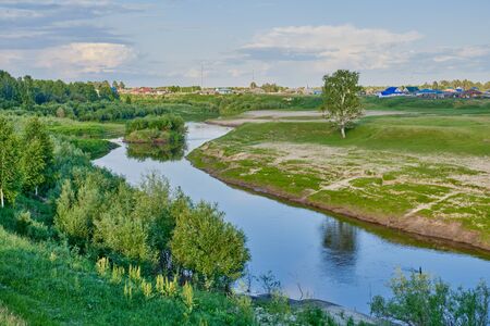 Summer landscape on a sunny day. Neighborhood of the Siberian village Begitino, Tyumen region, Russia. Vagai river, lonely birch and taiga forest standing on a meadow. Beautiful clouds in the sky.の写真素材