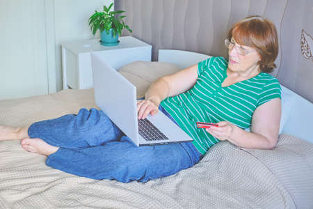 Senior woman using a laptop in her bedroom at home. Happy retired person shopping online on the bed. Lifestyle Copy spaceの写真素材