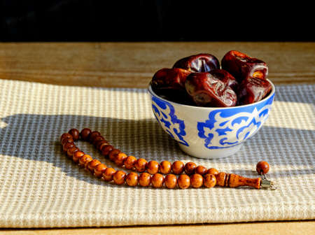 Cup with a traditional oriental pattern with dates and stone rosary on a napkin during sunset. The first meal, Muslim fast Eid al, Urazaの写真素材