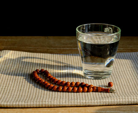 A glass of clear water, stone rosary on a napkin during sunset. The first meal, Muslim fast Eid al, Urazaの写真素材