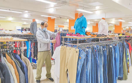 Mature man in mask choosing clothes at Second hand store. Conscious consumption, a new normal conceptの写真素材