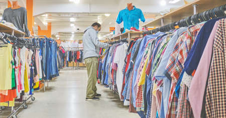Mature man in mask choosing clothes at Second hand store. Conscious consumption, a new normal conceptの写真素材