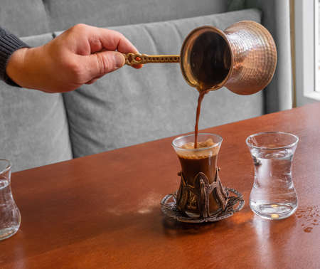 A male barista hand pouring fresh Turkish coffee from a turk into a beautiful oriental-style glass.の写真素材