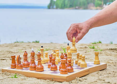 A hand of senior man making a move in a game of chess on background of the sandy beach near the...