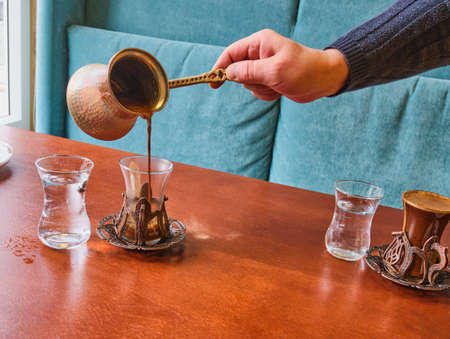 A male barista hand pouring fresh Turkish coffee from a turk into a beautiful oriental-style glass.の写真素材