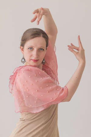 Attractive young caucasian woman dancing flamenco with beautiful arms in a pink beige dress, looking at the camera. Vertical portrait on a beige background.の写真素材