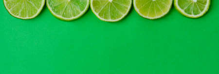 Halves of sliced limes on a green background. Banner Top viewの写真素材