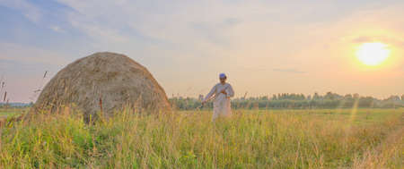At sunset an senior Muslim man in an embroidered skullcap and white traditional Clothes mows...