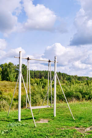 Summer rural landscape. A swing stands on a hill over the background of a forest and a beautiful cloudy sky. Country life conceptの写真素材