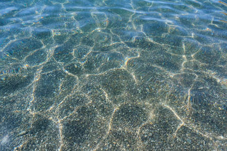 Abstract background of transparent sea water on the rocky beach with ripples and highlights of light.の写真素材