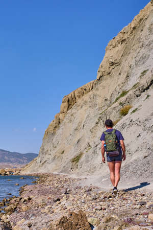 A tourist with a backpack walks along the path of the rocky coast of Cape Meganom on the Black Sea, Crimea peninsula.の写真素材