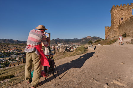 Sudak, Russia - September 15, 2020: The artist draws walls and towers of a medieval Genoese fortress on paper with brushes and paints. Sudak, Crimea peninsula.のeditorial素材