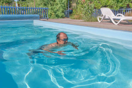 A middle-aged asian man swims in a pool in the courtyard of a house. Motion blurの写真素材