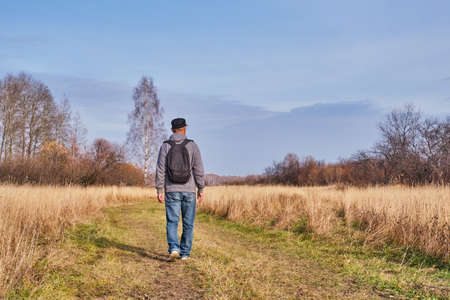 Active man in casual with backpack is walking in a meadow late autumn. Siberia, Russia. Single travel, new normal travel conceptの写真素材