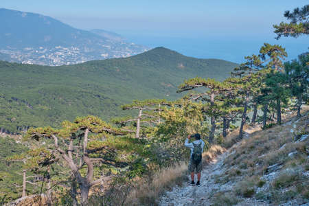 Beautiful landscape of the southern Crimea. Scenic slope of Ai Petri mountain. A man with a backpack is walking along the rocky mountain trail and taking a pictures by a smartphone.の写真素材