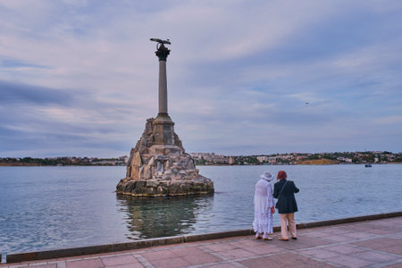 Sevastopol, Russia - September 28, 2020: Two elderly women friends are walking along the seaside promenade at sunset. The Monument to the Sunken Ships in Sevastopol Bay, 1905のeditorial素材
